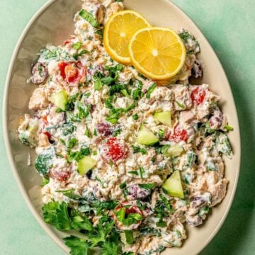 Close up of an oval serving platter with a veggie loaded Mediterranean tuna salad garnished with fresh herbs and lemon slices.