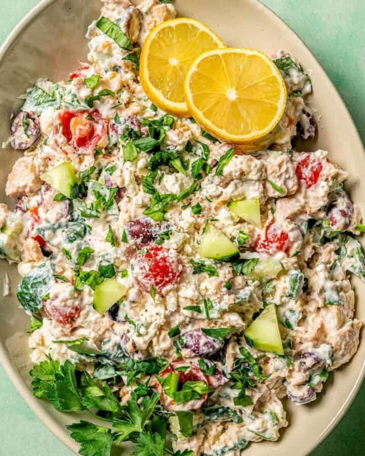 Close up of an oval serving platter with a veggie loaded Mediterranean tuna salad garnished with fresh herbs and lemon slices.