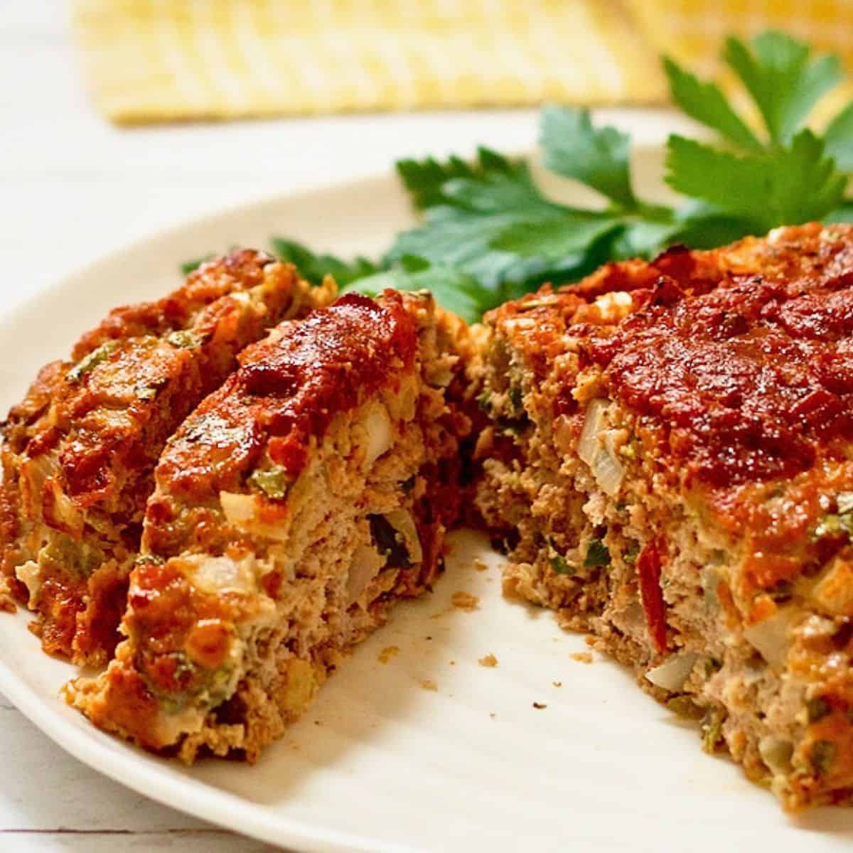 Close up of a sliced ground turkey Mexican meatloaf topped with salsa on a serving platter with fresh parsley as a garnish.
