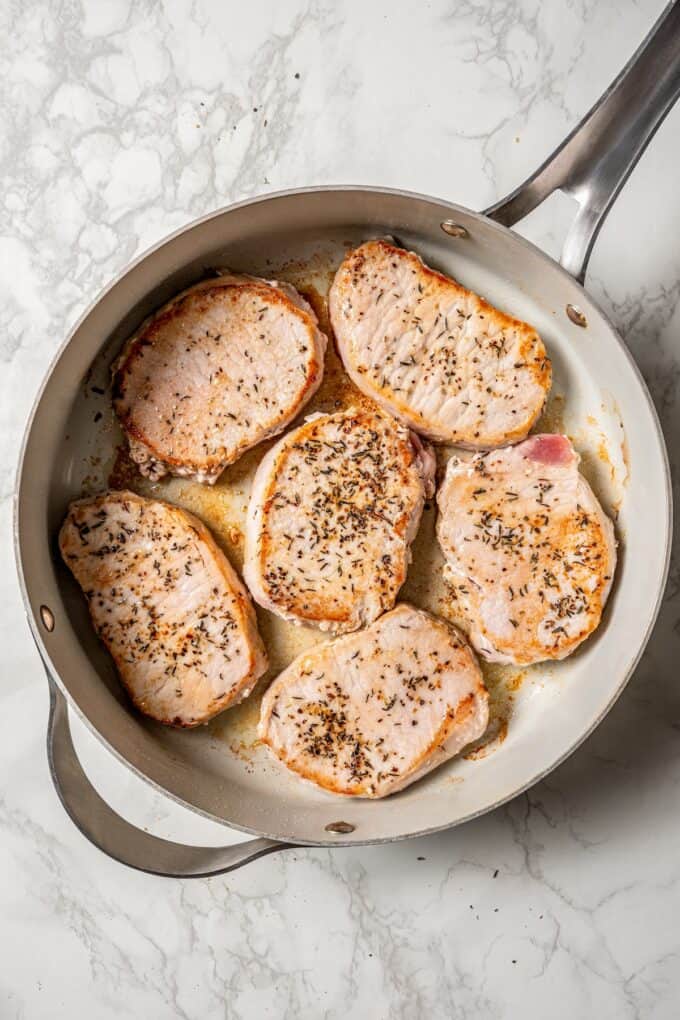 Six seared pork chops in a skillet.