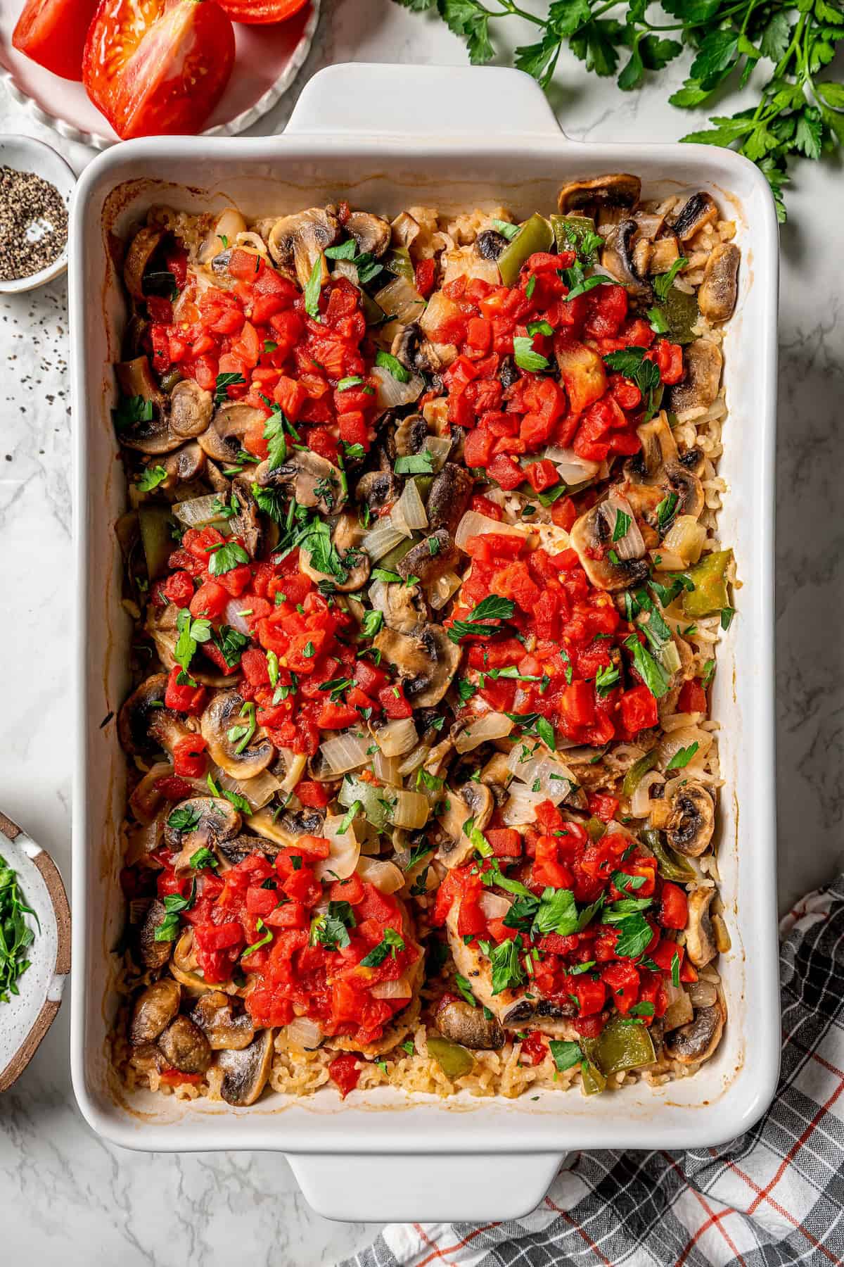 Pork chop casserole in a white baking dish with chopped fresh parsley on top and sprigs to the side for garnish.