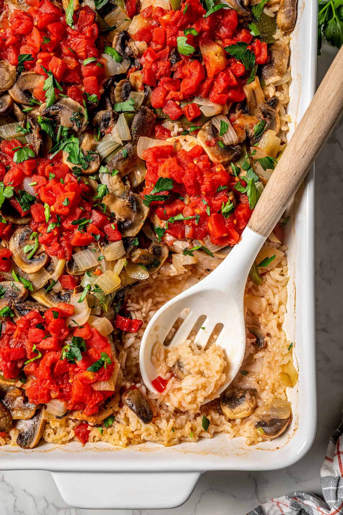 A serving spoon resting in a casserole dish of pork chops with rice and vegetables.