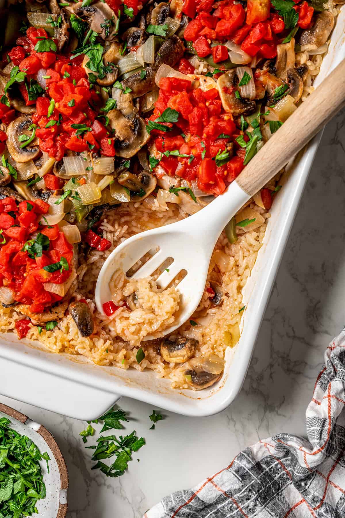 A slotted serving spoon resting in a baking dish of pork chop casserole.