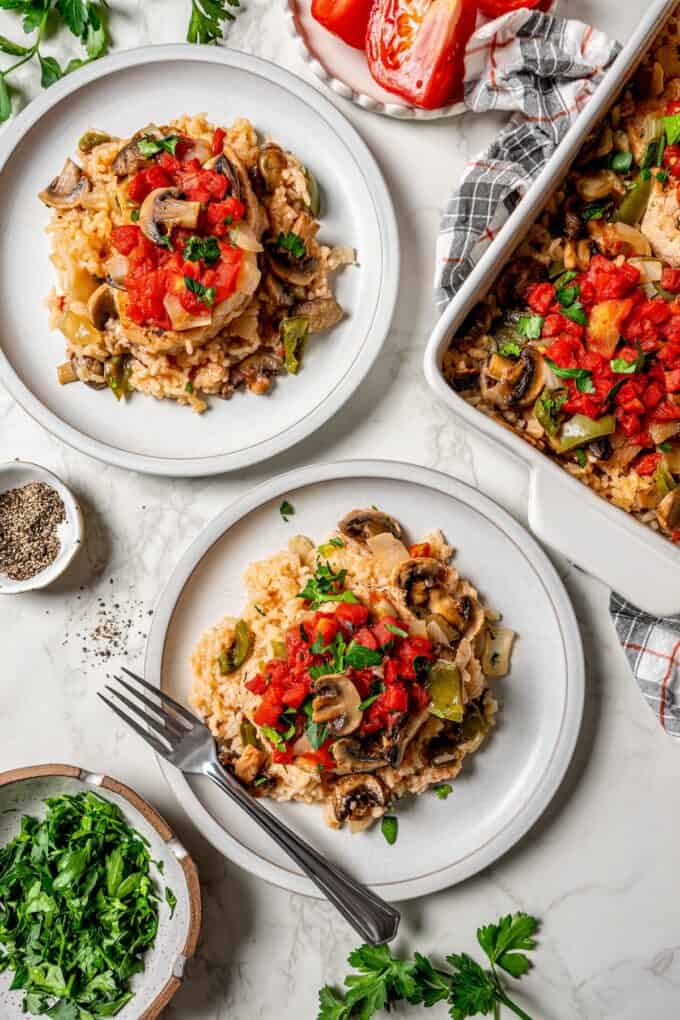Two plates alongside a casserole dish with pork chops and rice and vegetables and garnishes to the side.