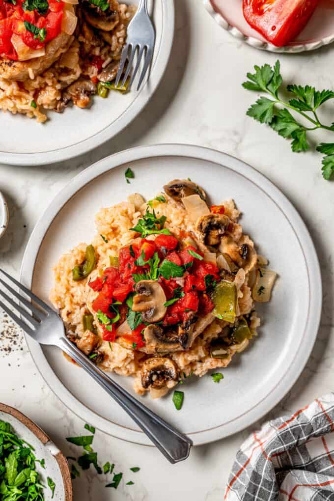A dinner plate with pork chop casserole served on it with parsley on top and to the side.