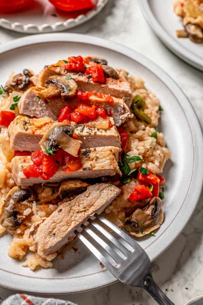 Close up of a sliced pork chop on top of cooked rice on a dinner plate with a fork resting on it.