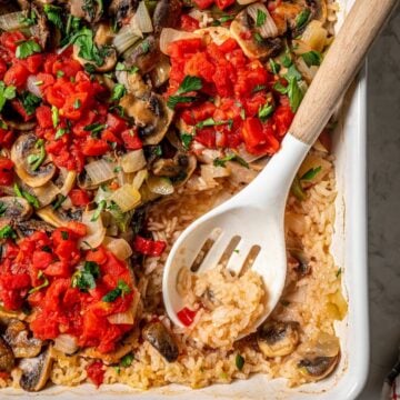 Close up of a slotted serving spoon resting in a casserole dish of pork chops with rice and vegetables.