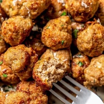 Close up of a meatball with a bite taken out on a fork that's resting in a platter of meatballs.
