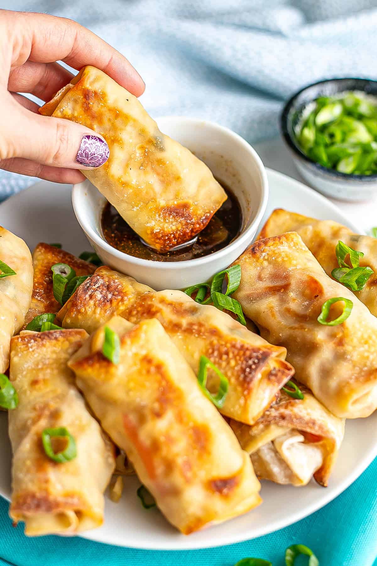 A hand dipping an egg roll into a small bowl of dipping sauce.