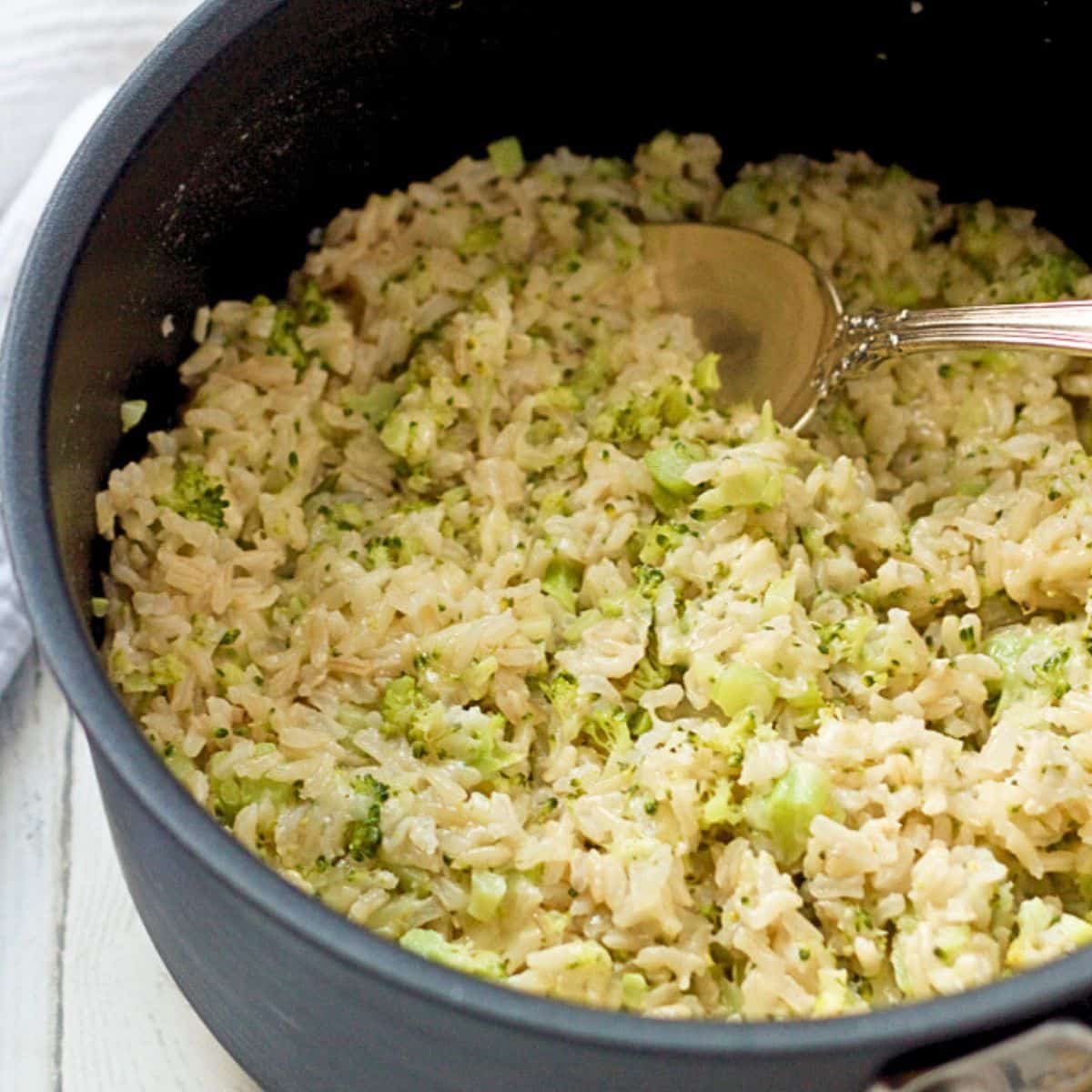 A dark pot filled with broccoli cheese brown rice with a spoon resting in it.