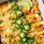 Baked cream cheese chicken enchiladas in a casserole dish with slices of jalapeños, lime and chopped fresh green onions on top and a text overlay on the photo.