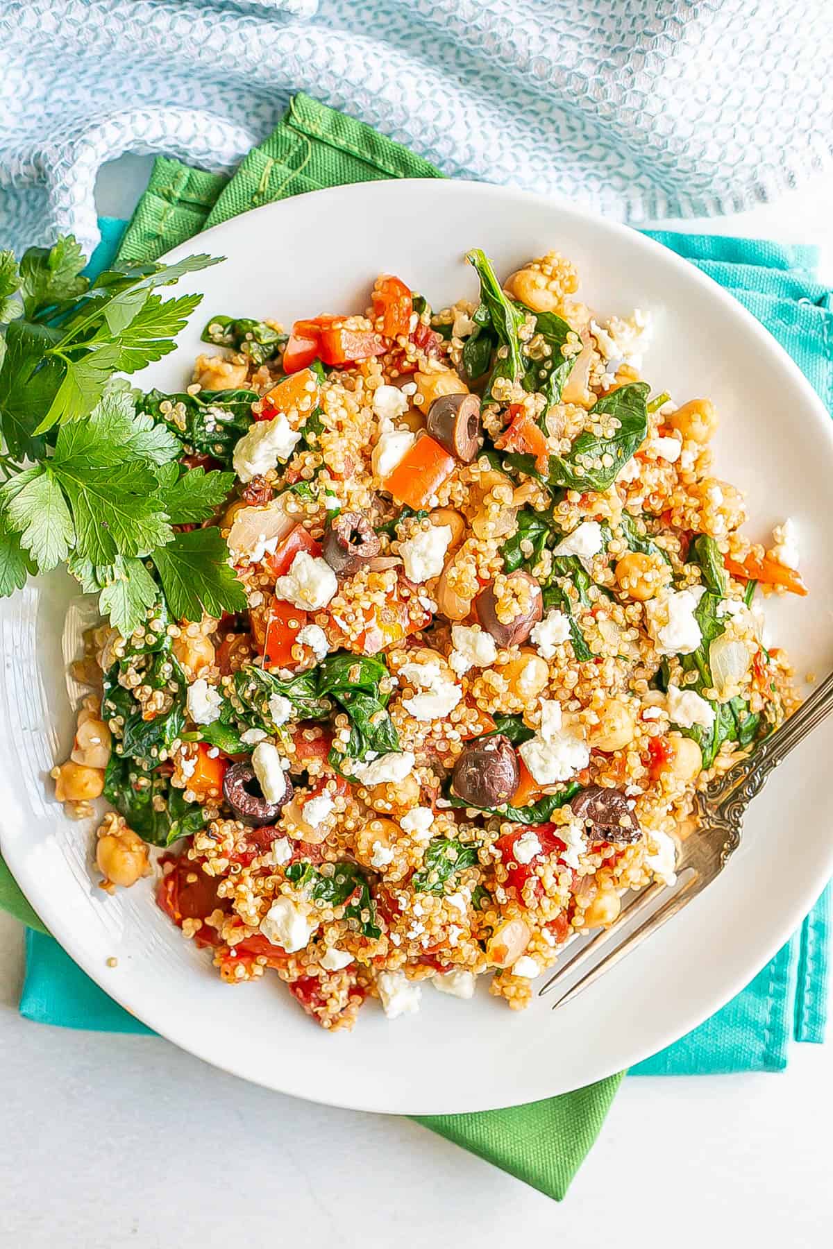 A vegetarian quinoa mixture with chickpeas, spinach, tomatoes, olives and feta cheese on a white plate.