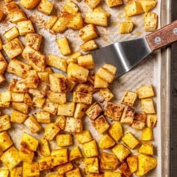 Close up of a small spatula scooping up roasted parsnips from a sheet pan.