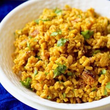Close up of a curried brown rice salad with golden raisins and cilantro served in a white bowl.