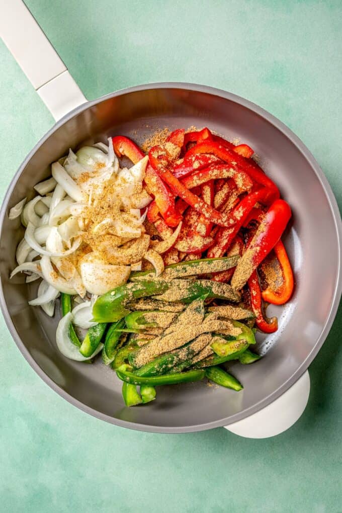 A skillet with groups of onion, red pepper and green pepper with fajita seasoning sprinkled on top.