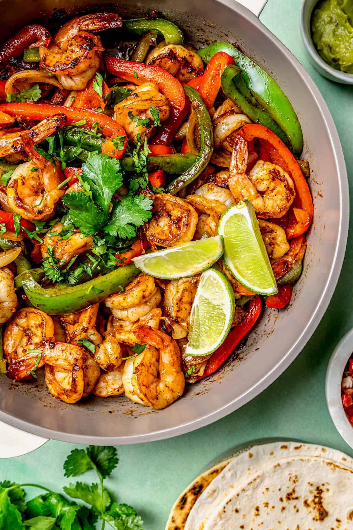 Close up of a shrimp skillet with peppers and lime wedges.