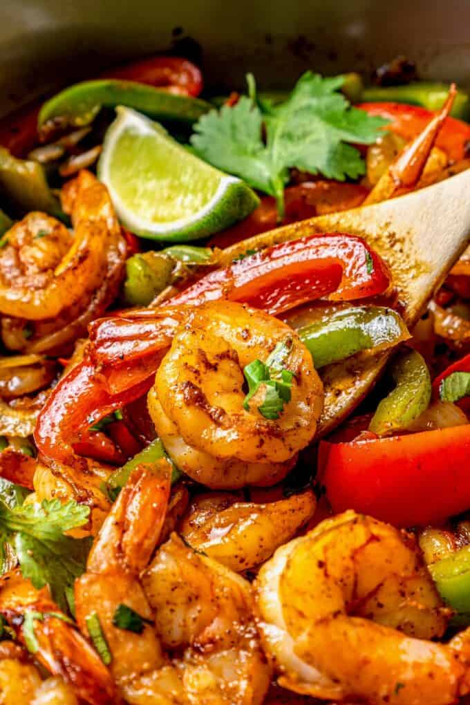 Close up of a spoon full of shrimp with peppers in a skillet of fajitas.