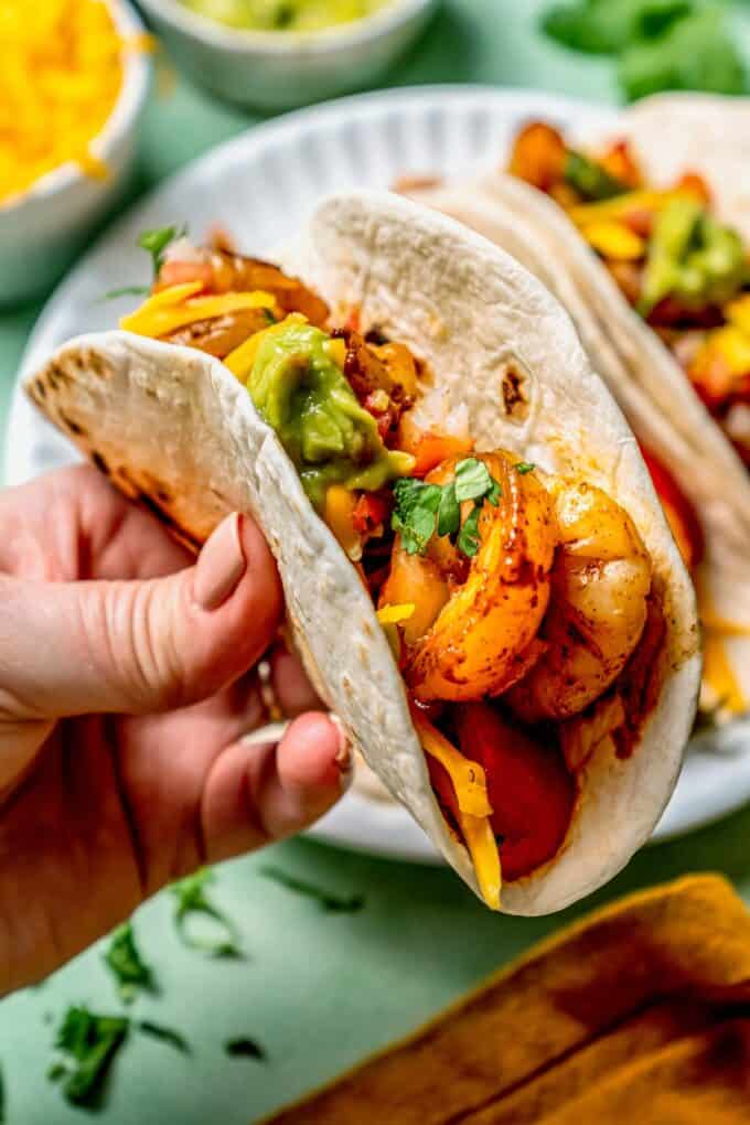 A hand holding up a shrimp fajita in a flour tortilla.