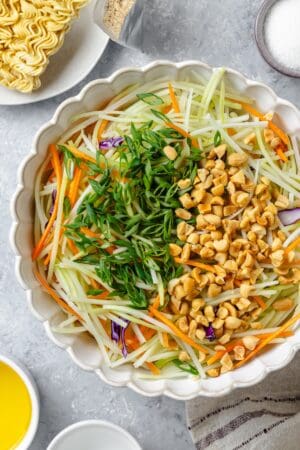 Peanuts and sliced green onions on top of broccoli slaw in a large bowl.