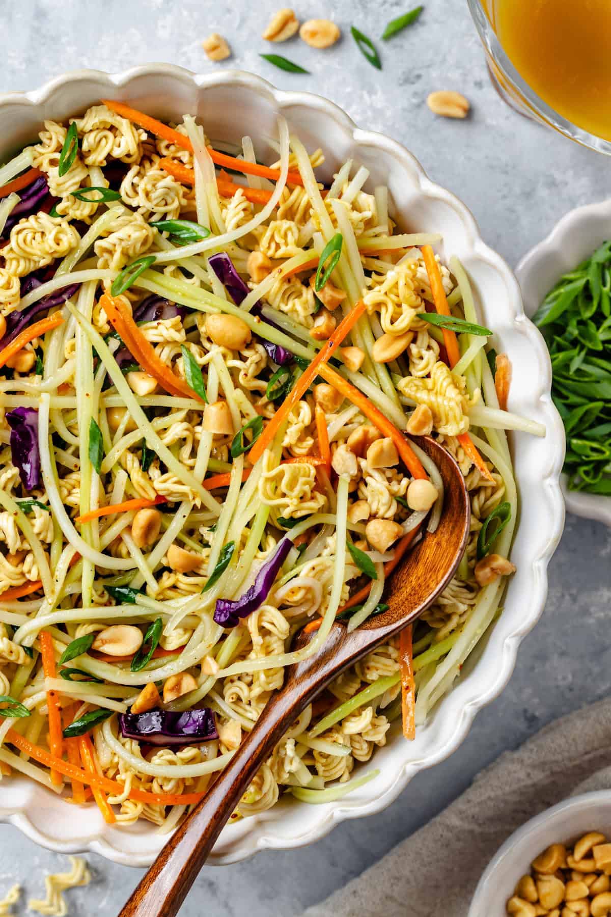 Close up of a wooden spoon in a serving bowl with an Asian style slaw with ramen noodles and peanuts.