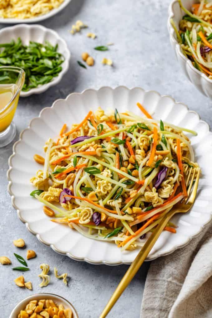 A gold fork resting on the side of a plate with a ramen and broccoli slaw salad.