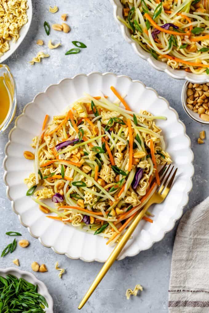 A fork resting on a plate with a serving of a crunchy ramen noodle coleslaw.