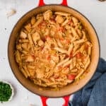 Cajun chicken pasta in a red stock pot with plates, forks, bread and parsley nearby with a text overlay on the photo.