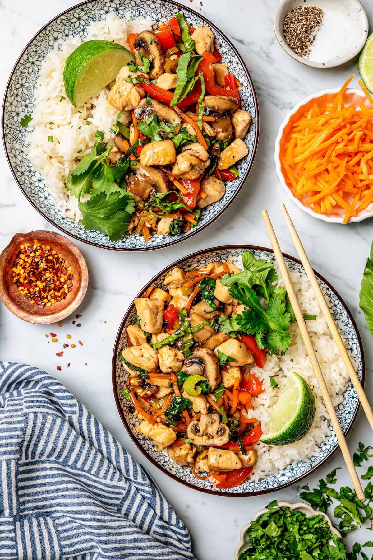 Two bowls of rice alongside a chicken, bok choy and vegetable stir fry with cilantro and lime wedges on top.