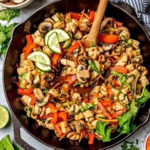A wooden spoon with a scoop of vegetables in a cast iron skillet full of a chicken stir fry.