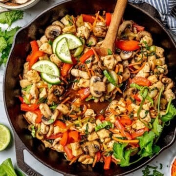 A wooden spoon with a scoop of vegetables in a cast iron skillet full of a chicken stir fry.