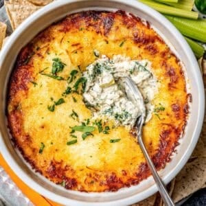 Close up of a ramekin with a baked spinach artichoke dip and a spoon scooping into it.