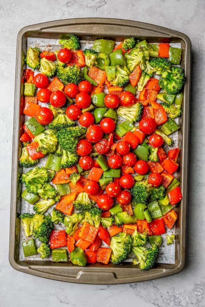 A sheet pan of roasted vegetables, including broccoli, green and red bell peppers and tomatoes.