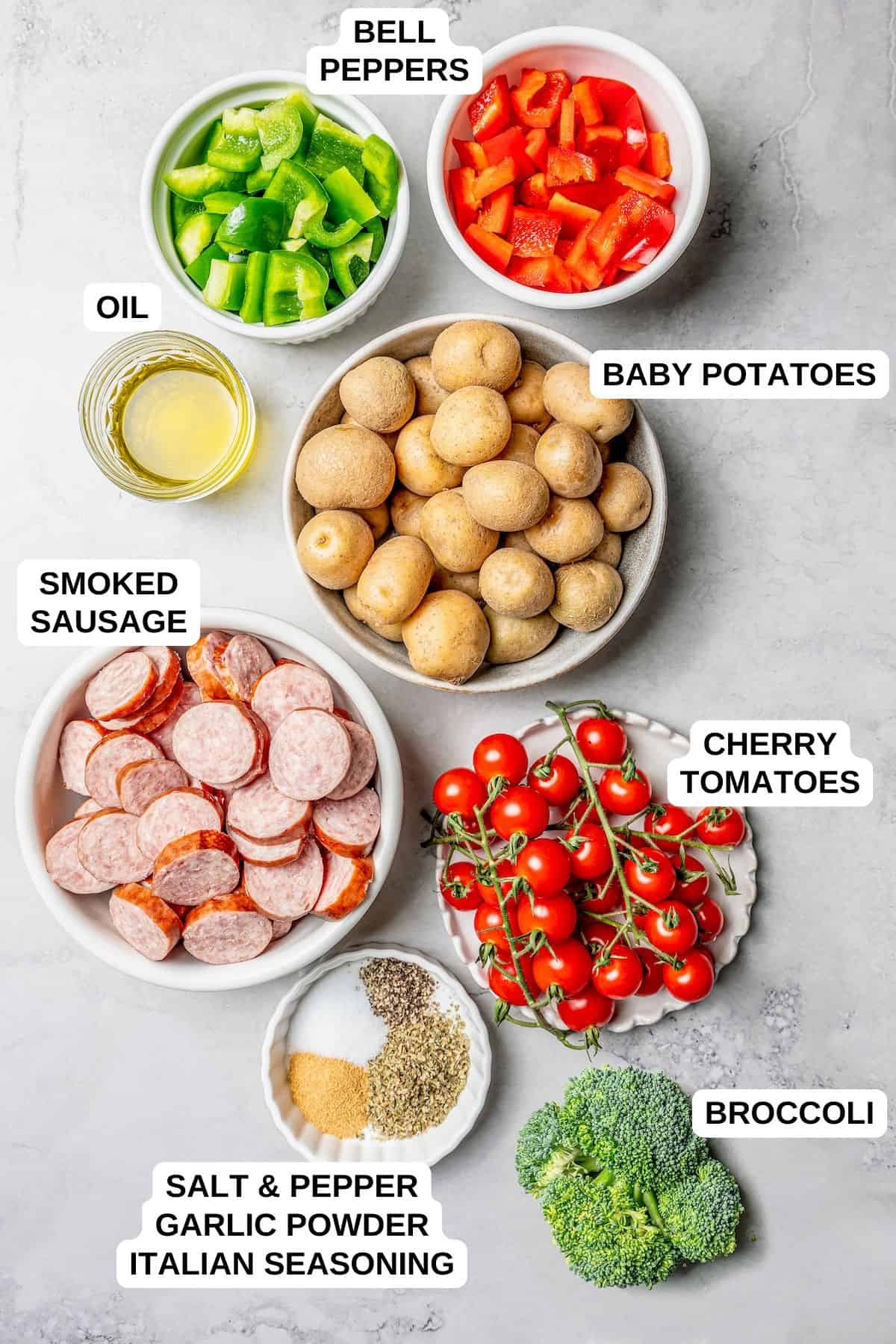 Ingredients laid out in separate containers and labeled, including smoked sausage, baby potatoes, bell peppers, tomatoes and broccoli.