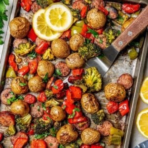 Close up of a spatula scooping up some roasted veggies and sausage from a sheet pan dinner.
