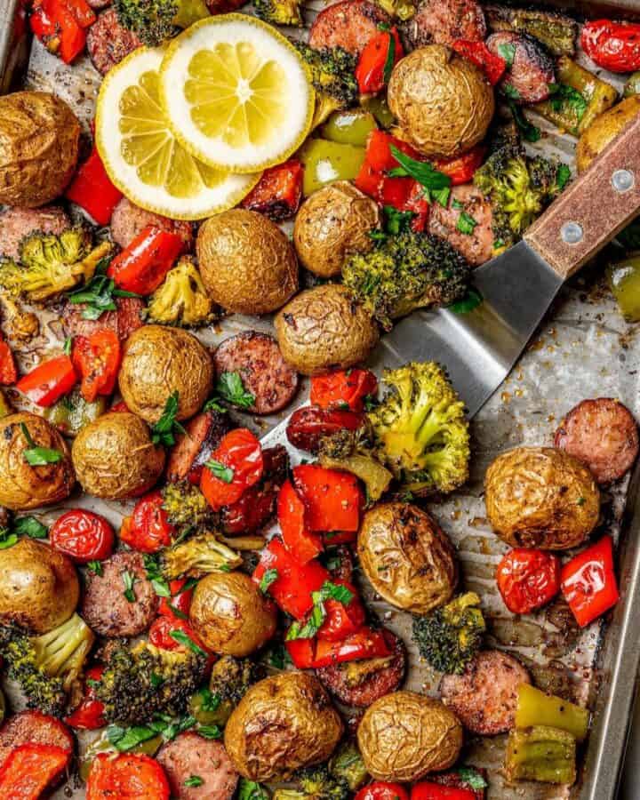 Close up of a spatula scooping up some roasted veggies and sausage from a sheet pan dinner.