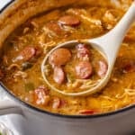 A spoon scooping up a sausage and chicken gumbo from a large stock pot with a text overlay on the photo.