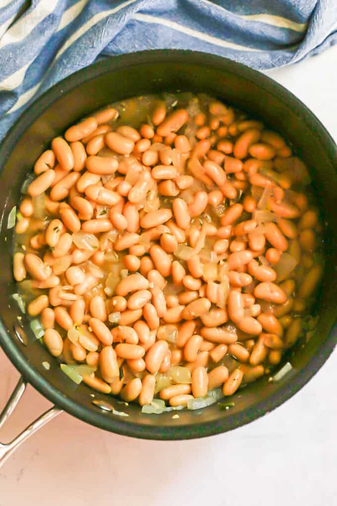 Cannellini beans cooking in a saucy mixture with onions in a large pot.