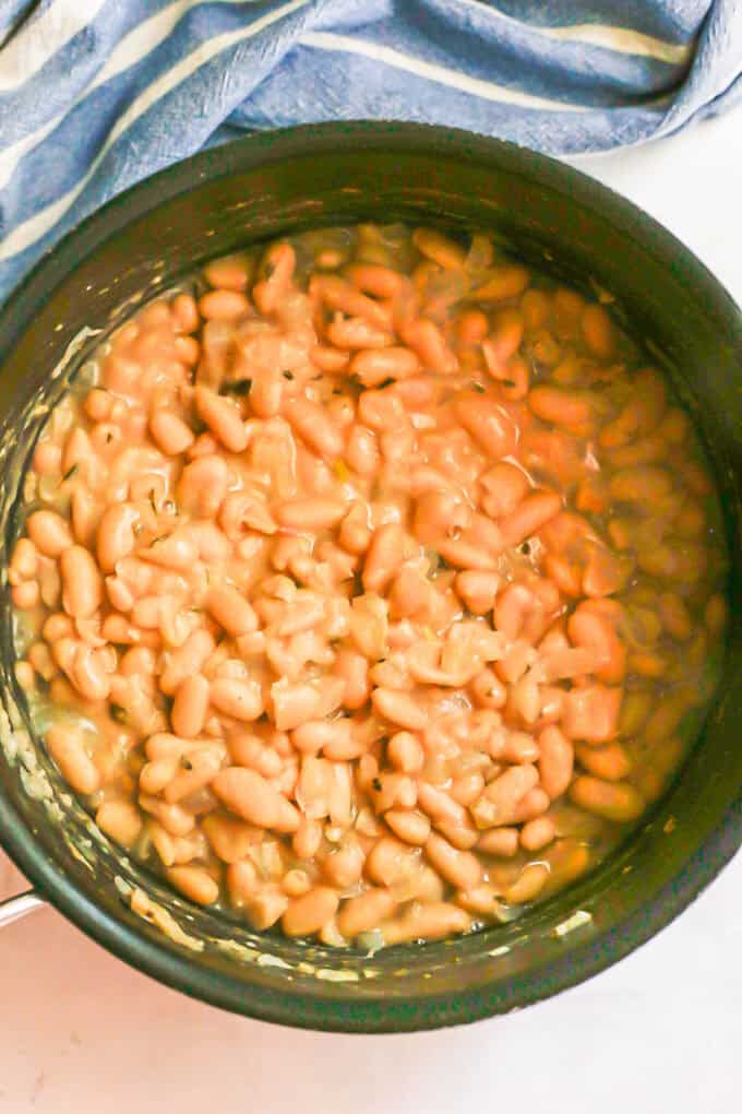 Partially mashed cannellini beans cooking with onions in a large pot.