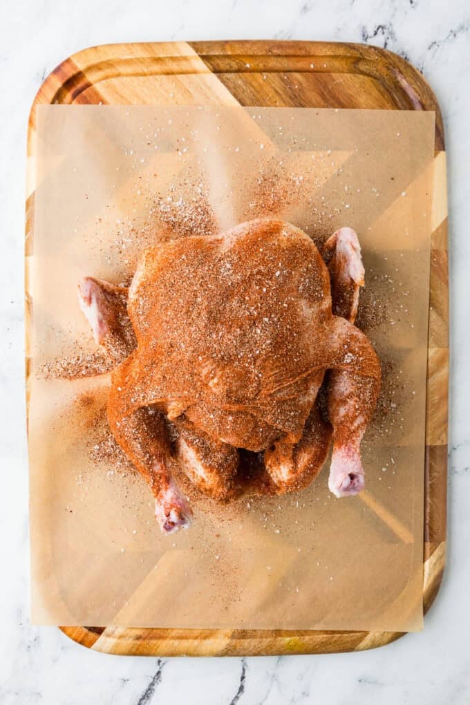 A whole chicken on a cutting board covered in a seasoning mixture.