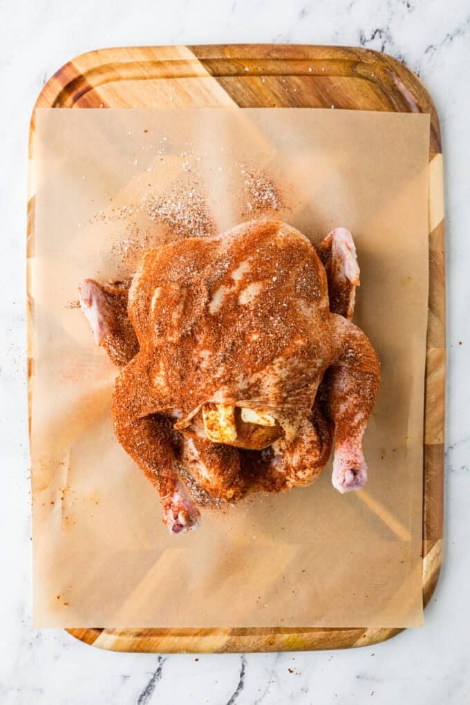 A whole chicken on a cutting board covered in a seasoning mixture and stuffed with butter.