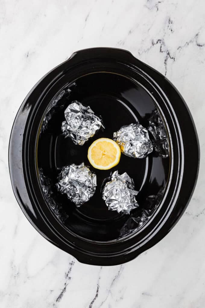A crock pot insert with a half lemon and 4 balls of aluminum foil in the bottom.