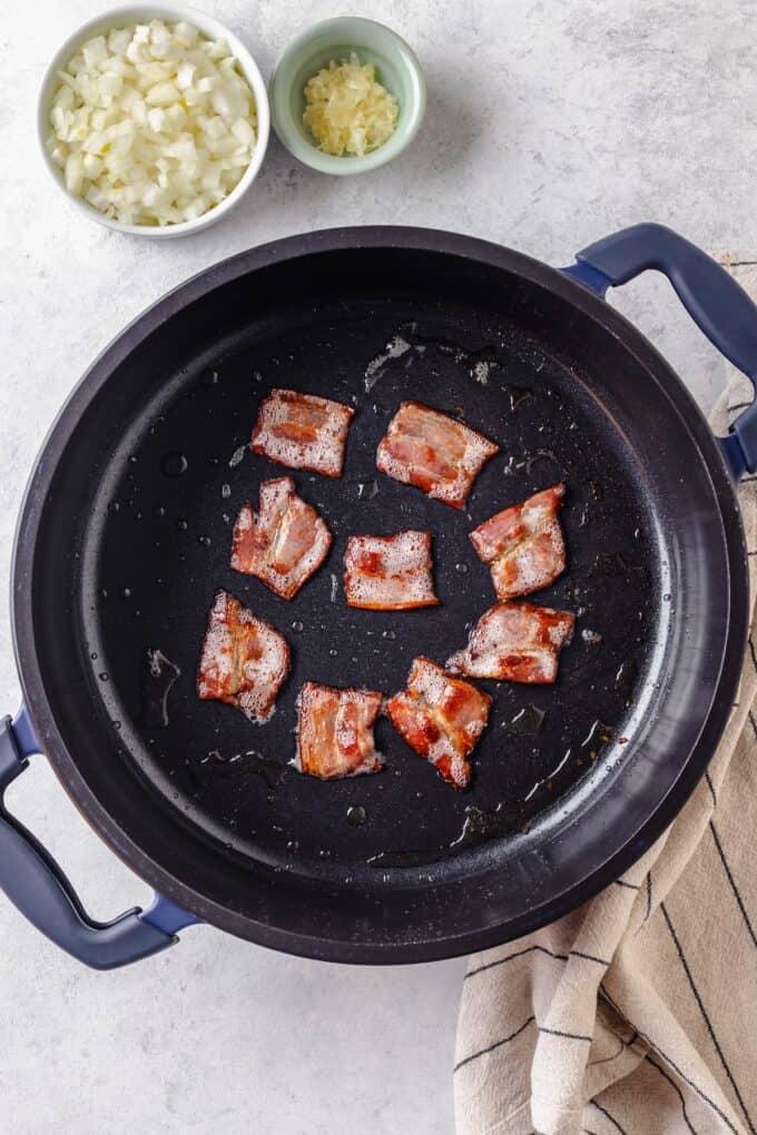 Pieces of bacon cooking in a large deep pot.