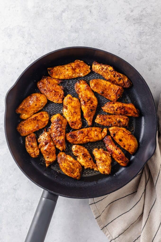 Cooked, seasoned strips of chicken in a dark skillet.