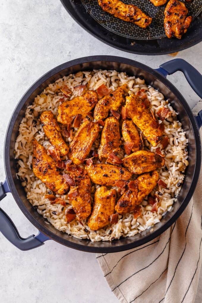 Seasoned cooked chicken strips atop a pot of rice with black eyed peas.