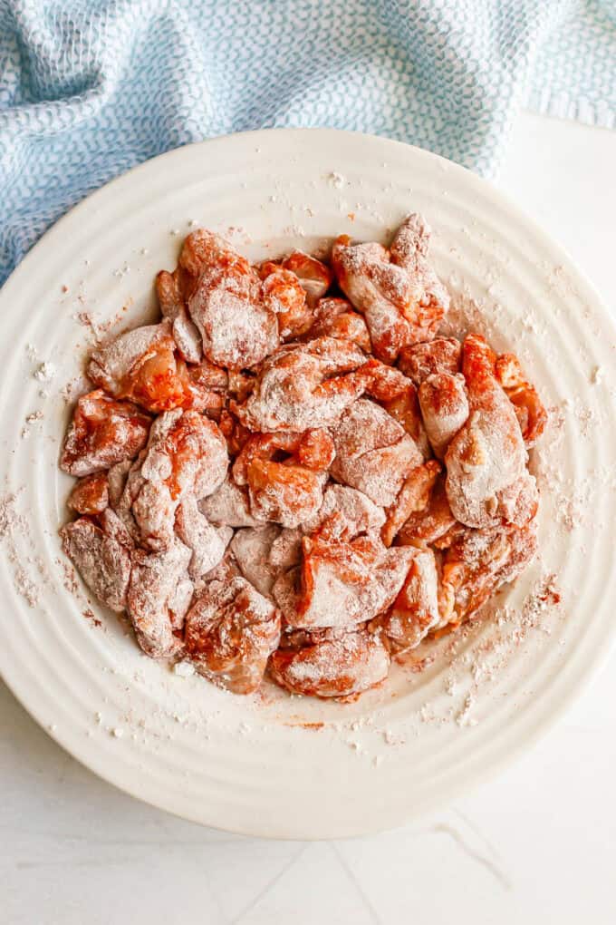 Cubed pieces of chicken thighs in a white bowl with a paprika seasoning and tossed in flour.