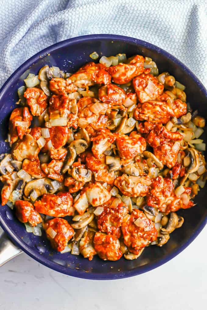 A large dark skillet with cooked pieces of paprikash chicken mixed with onions and mushrooms.