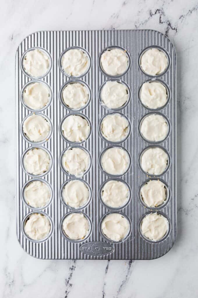 A mini muffin tin with a cheesecake filling over a graham cracker crust.