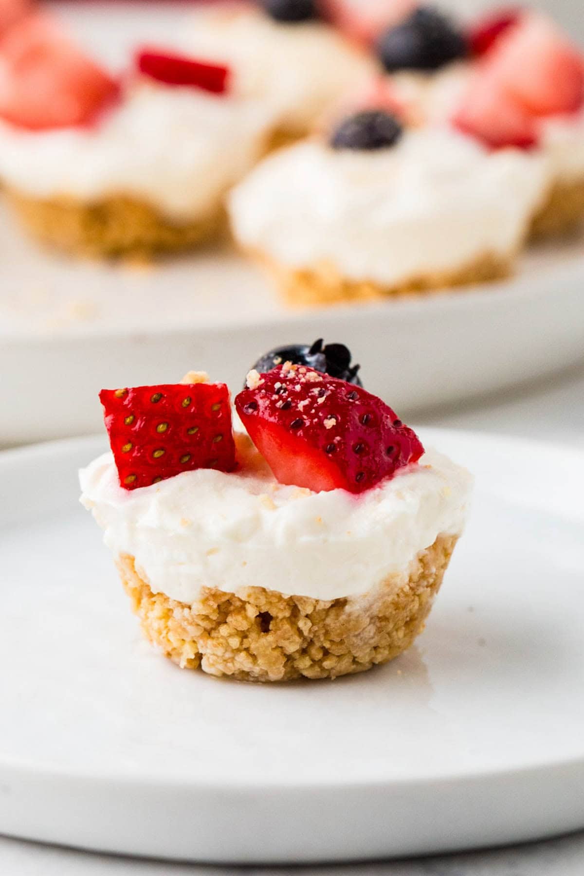 An individual graham cracker crust mini cheesecake with fresh berries on top served on a small white plate.