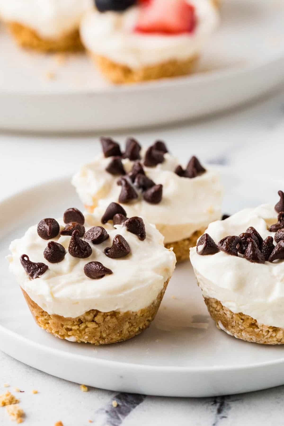 Three mini cheesecakes with a graham cracker crust and mini chocolate chips on top on a small white plate.