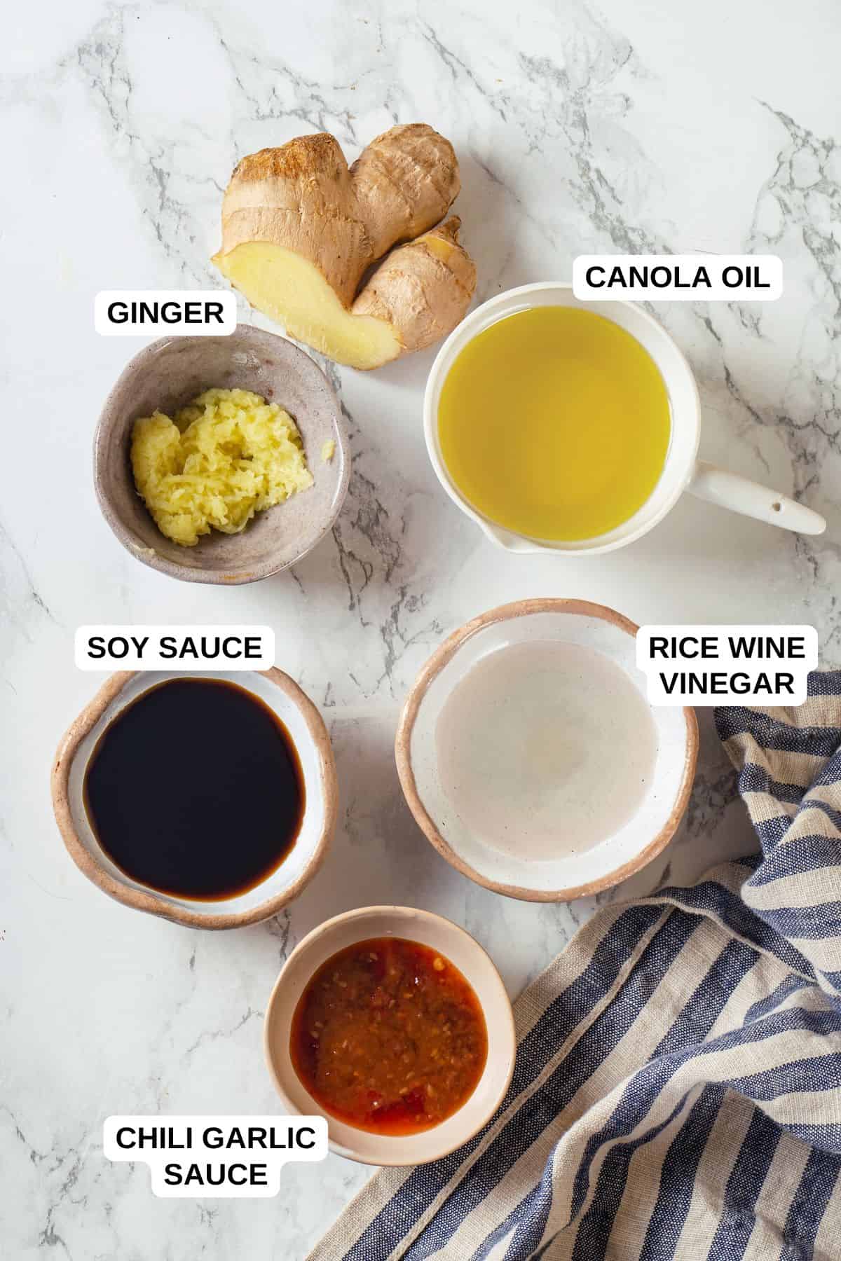 Ingredients laid out in separate containers for making a homemade vinaigrette with soy sauce, ginger, oil, rice wine vinegar and chili garlic sauce.